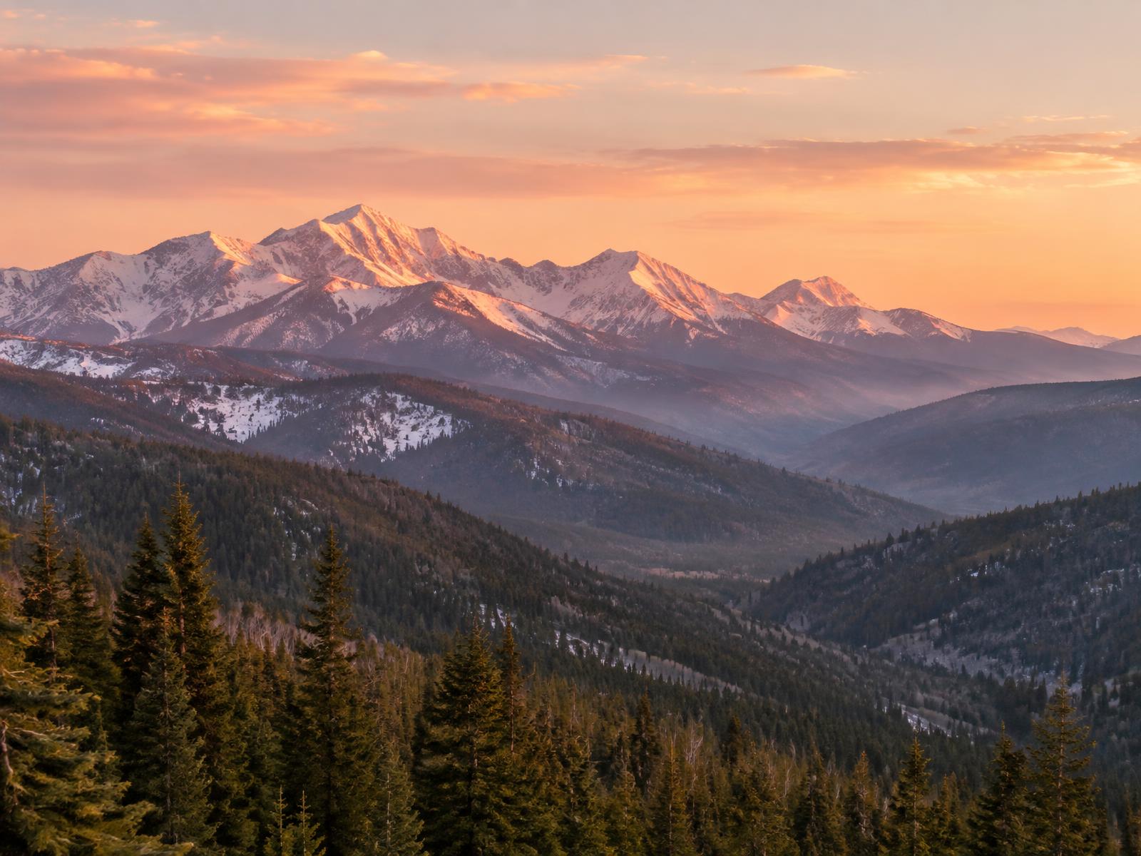 Golden sunrise lighting snow-covered mountain peaks above forested valleys